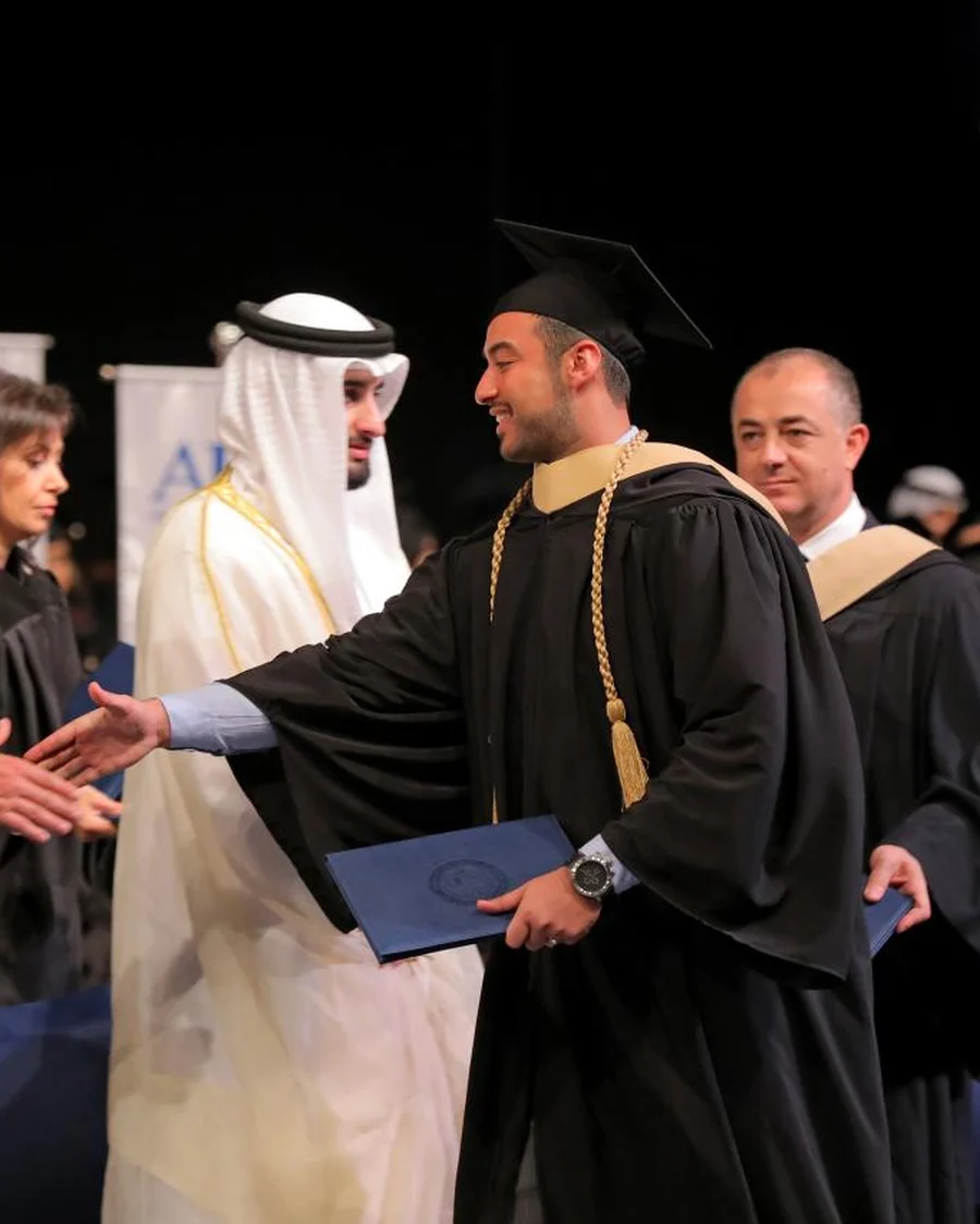 Ali Owji crossing the stage at graduation to shake hands, wearing cap and gown.